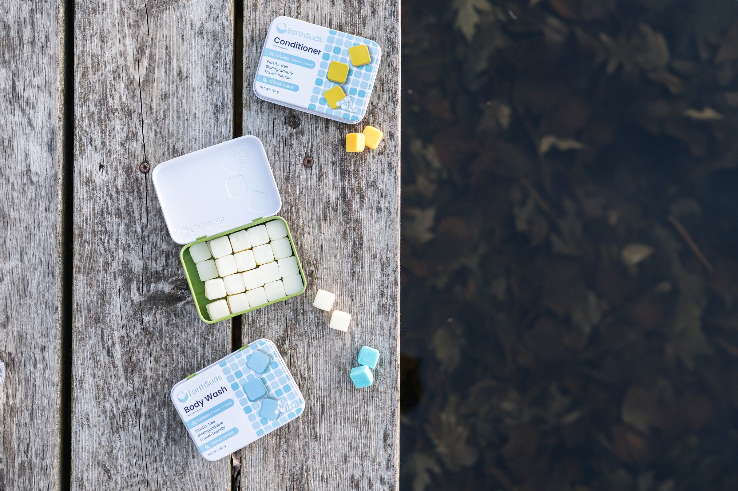 Sustainable shampoo, conditioner, body wash tablets on a dock beside plastic-free cases that are eco-friendly and biodegradable. Natural travel-friendly shampoo, conditioner, and body wash with clean ingredients that are paraben-free and phosphate-free.